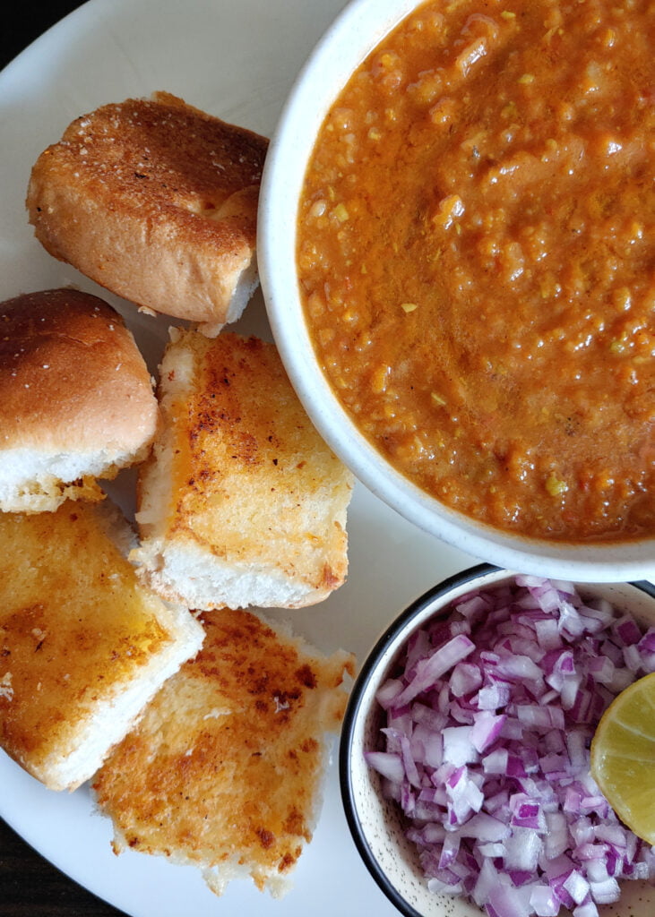 close look of pav bhaji served on a plate with onions and lemon wedges