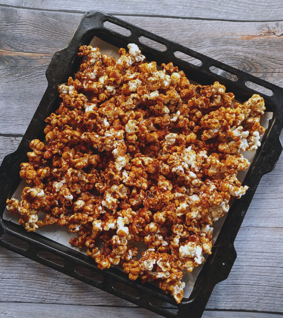 caramel coated popcorn spread out in a large tray to cool down