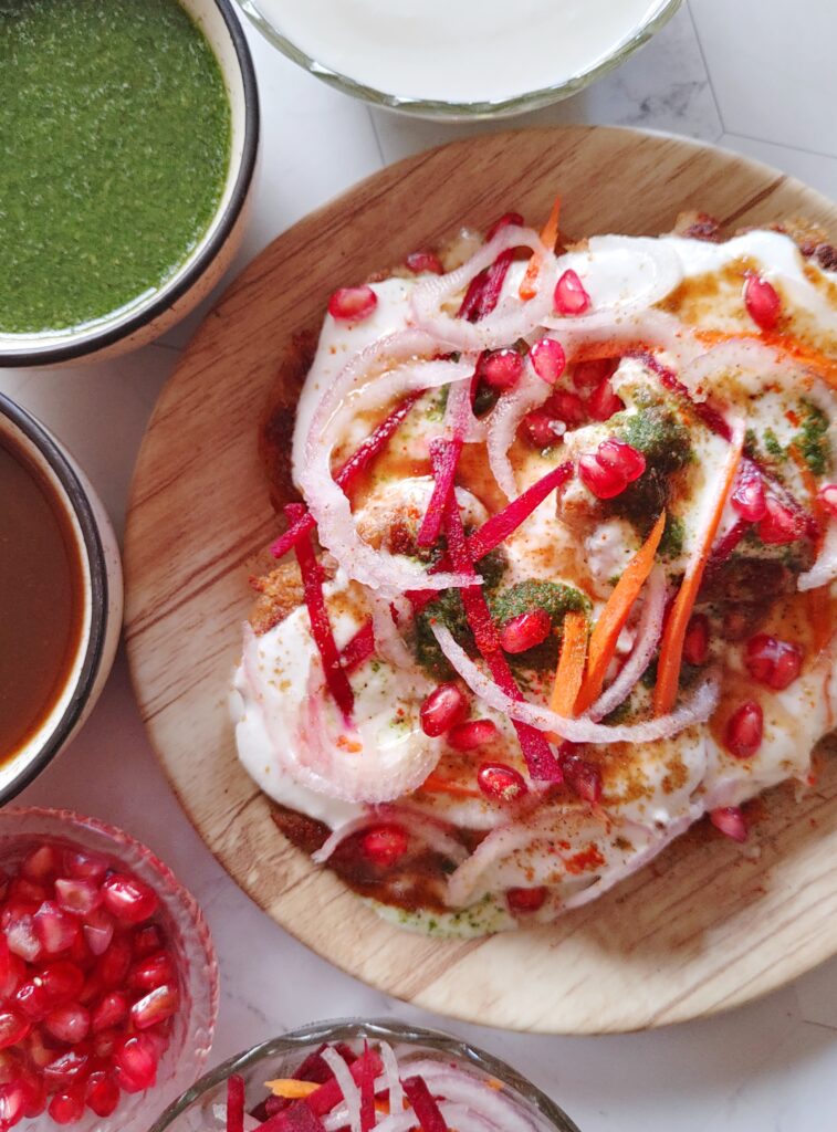 aloo tikki chaat served in a plate with sauces , curd and garnishes on the side