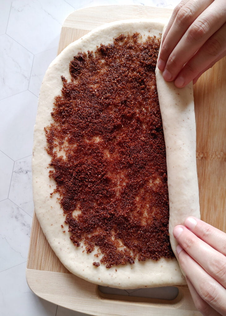 cinnamon roll cookies with cinnamon and brown sugar filling spread over the flattened dough now rolling to form a log shape