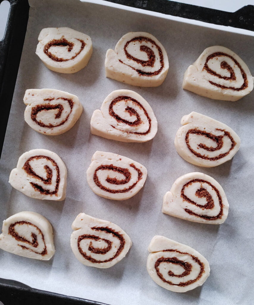 cinnamon roll cookies with cinnamon and brown sugar filling spread cut into pieces and placed on baking sheet before baking