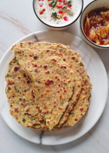 methi parathas in a plate served with sweet mango pickle and raita with one paratha folded