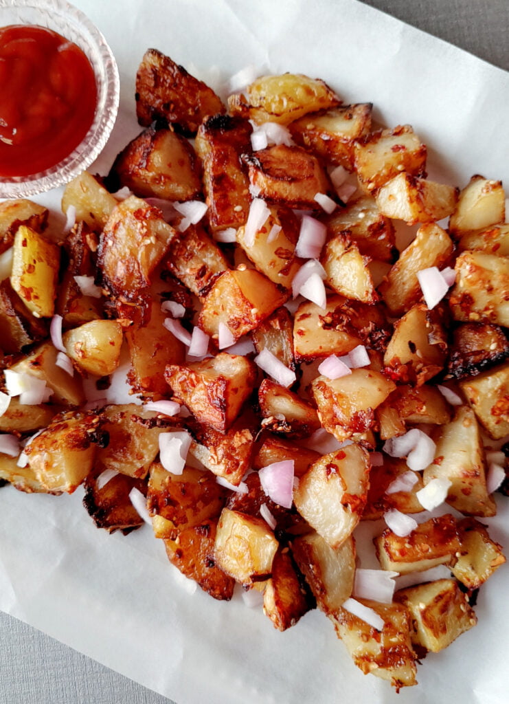 chilli oil glazed roasted crispy potatoes served in a platter with ketchup and garnished with raw onions