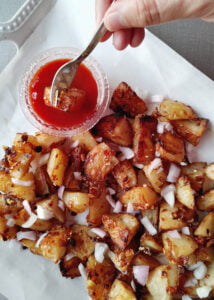 featured image of chilli oil glazed roasted crispy potatoes served in a platter with ketchup and raw onions sprinkled on the top
