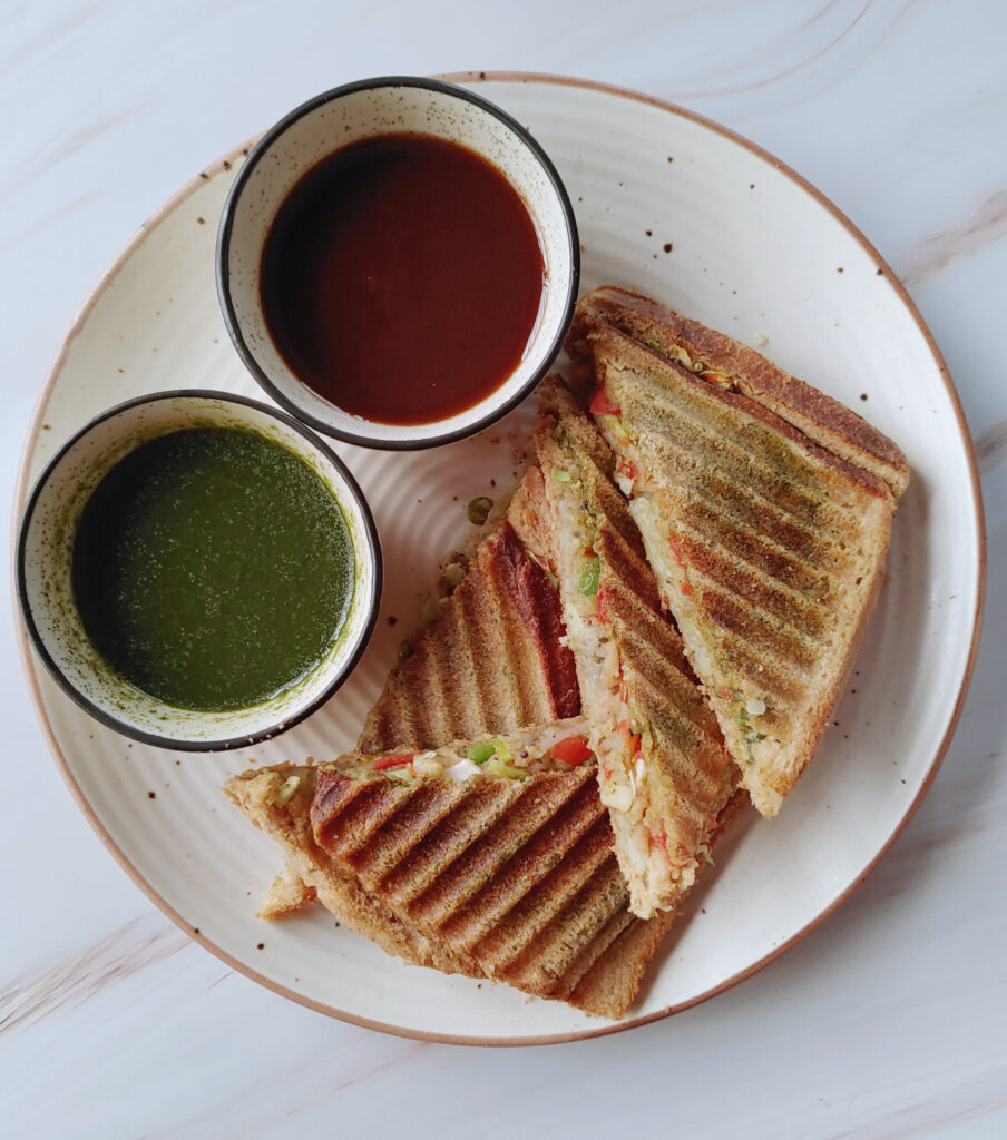 potato veg grilled sandwich served in a plate along with sweet tamarind and mint coriander chutneys