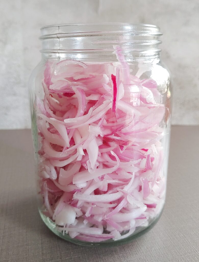 sliced red onions in a glass or mason jar