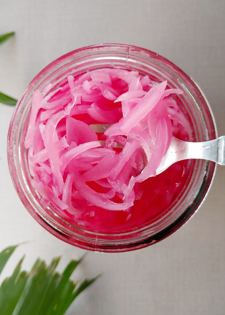 pickled red onions in a glass jar taken out with a fork
