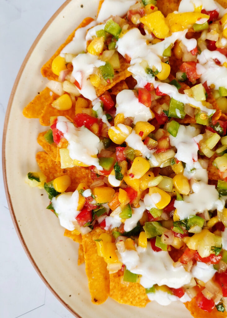 photo from left side of mango salsa spread over nachos with yogurt dip drizzled over nachos in a plate