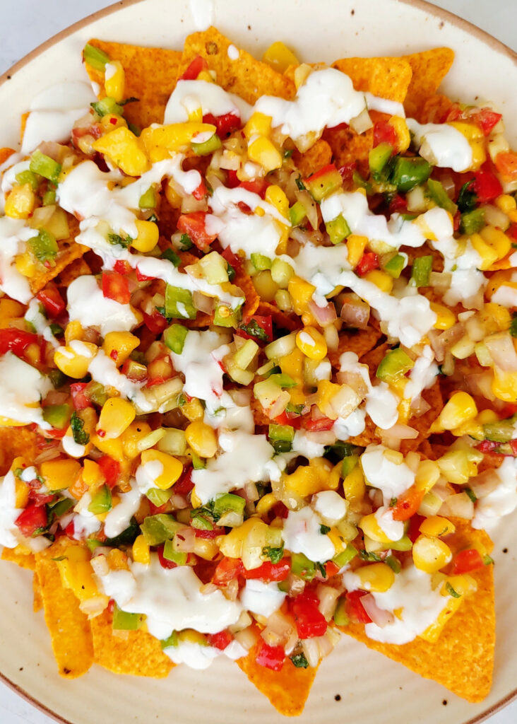 zoomed in photo of mango salsa spread over nachos with yogurt dip drizzled over nachos in a plate
