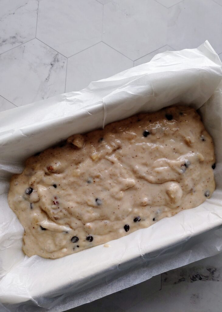 eggless chocolate chip walnut banana bread batter spread in a parchment lined loaf pan